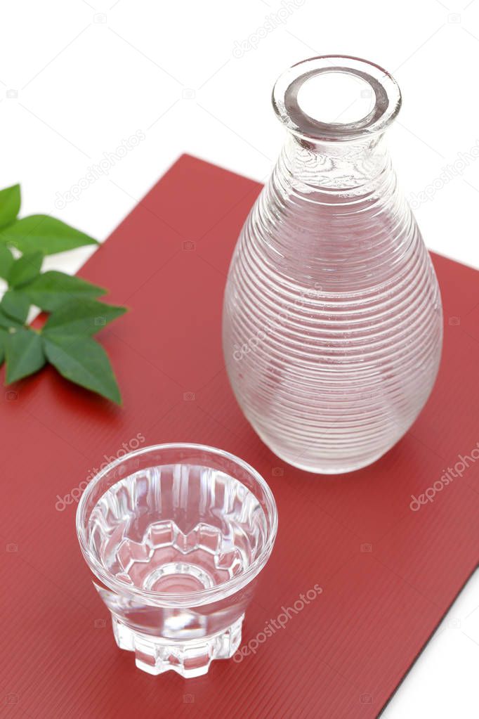 Japanese sake in transparent glass cup and jar on red background