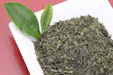 kırmızı arka plan üzerinde yeşil çay yaprakları ile kurutulmuş çay yaprakları 