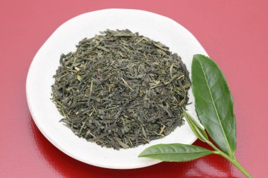 kırmızı arka plan üzerinde yeşil çay yaprakları ile kurutulmuş çay yaprakları