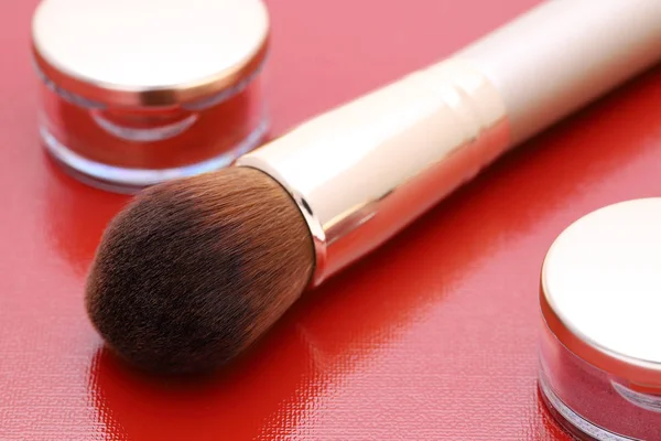 closeup of a make up powder and a brush on red background