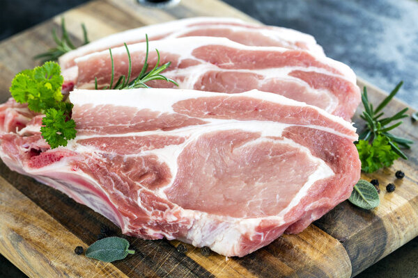 Raw pork chops on chopping board, with fresh herbs and spices.