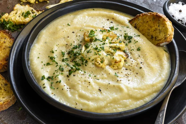 Soupe au chou-fleur dans un bol noir rustique — Photo