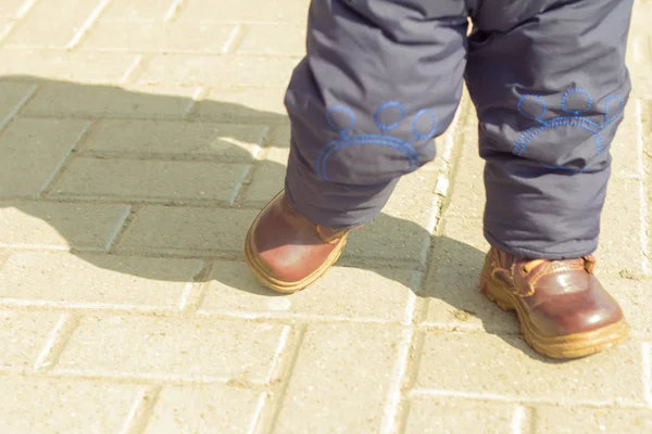 a small child in boots walks on the street in the spring on a Sunny day