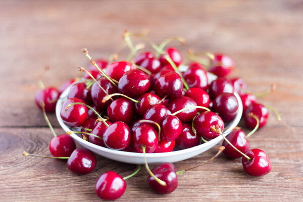  fresh ripe cherries in a plate on a wooden table