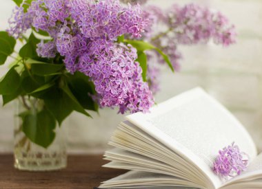 Çiçek açan leylak demeti ve masanın üstünde açık bir kitap.