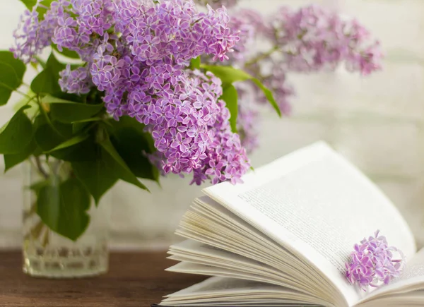 Çiçek açan leylak demeti ve masanın üstünde açık bir kitap.