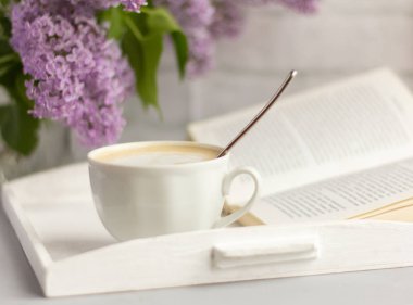 süt ile sıcak kahve bir fincan, leylak bir buket ve masada açık bir kitap, dinlenme zamanı