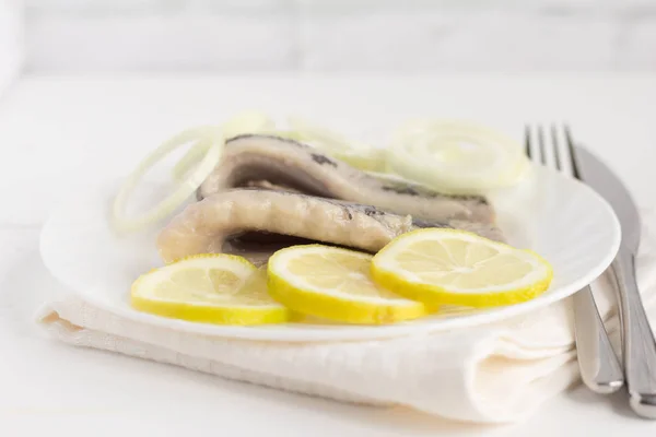 白を基調としたホワイトプレートにレモンと玉ねぎとおいしい柔らかいニシンの切り身 — ストック写真