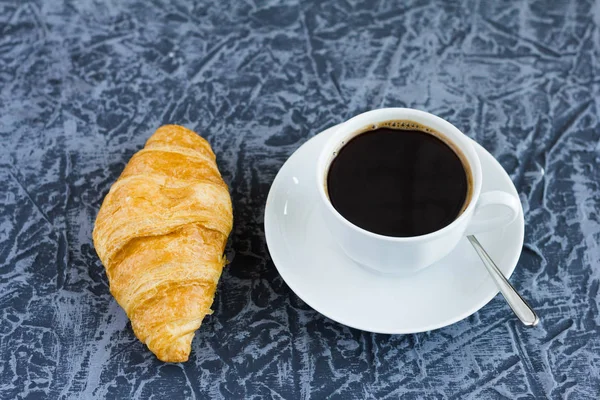 Eine Tasse schwarzen Kaffee und ein Croissant auf dem Tisch — Stockfoto