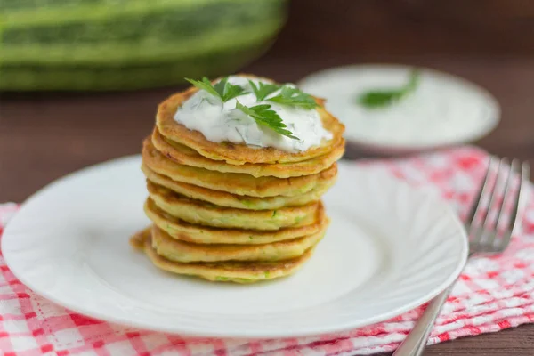 delicious homemade zucchini pancakes with sour cream and herbs on a wooden background