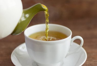 Sıcak yeşil çay ahşap bir masa üzerinde beyaz bir Fincan içine dökülür