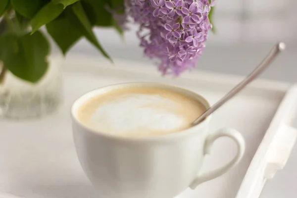 Secangkir kopi panas dengan susu dan karangan bunga lilac di atas meja — Stok Foto