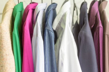 Yakın - farklı giysiler ile askıları kadar. Askıda asılı farklı renklerde gömlek ve ceketler