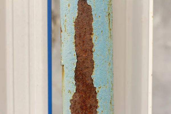 a rusty metal pole with blue paint falling off