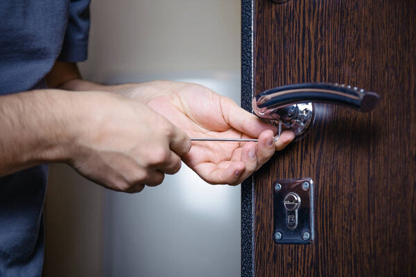 Close-up of male hands repairing or replacing an entrance door lock with a hex screwdriver. Increased house protection from burglars.