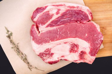 Tahta kesme tahtasının üzerinde çiğ biftek ve baharat. Restoranlar için taze malzemeler. Kemikte et.