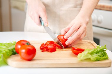 Tahta kesme tahtasıyla sulu kırmızı domatesleri ikiye bölen genç bir kızın zarif elleri. Malzeme ve sebze hazırlığı. Diyet, beslenme, sağlıklı yaşam tarzı için organik ürünler.