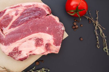 Baharatlı, otlu ve sebzeli taze çiğ biftek. Et kemiğin üzerinde. Kekik, karabiber, domates, siyah taşta sığır eti. Yemek arkaplanı. Mesaj için yer var. en üstteki görünüm.