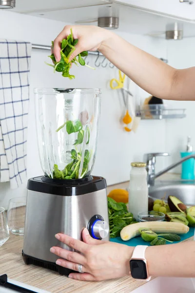 Kız elleri yeşil bir smoothie hazırlar, taze ıspanak yapraklarını karıştırıcıya koyar. Sağlıklı beslenme konsepti. Vejetaryenlik, vejetaryen yiyecekler, fitness yemekleri, detoks, gençlik koruma.