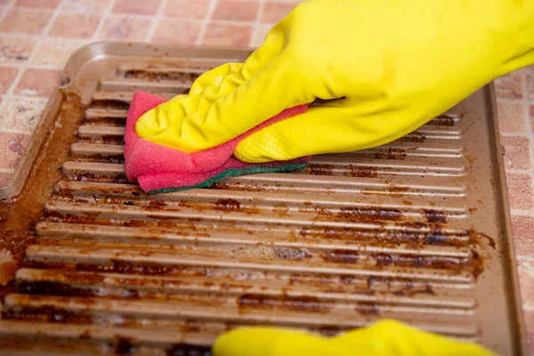 Cleaning the grill. Hands in yellow gloves clean the dirty grill of grease and burns with a cleaning agent. electric grill hygiene, cleaning contaminants with grill grates