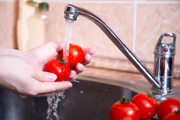 Lavaboda terli suyun altında sebze yıkamak. Sert eller sulu kırmızı domatesleri tutar. Hijyen konsepti, sebze hazırlama. Rutin mutfak işleri..