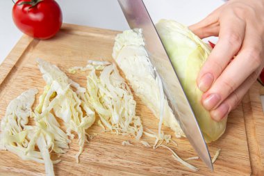 Close-up of a hand cutting fresh cabbage with a sharp knife on a wood cutting board, food preparation, healthy cooking