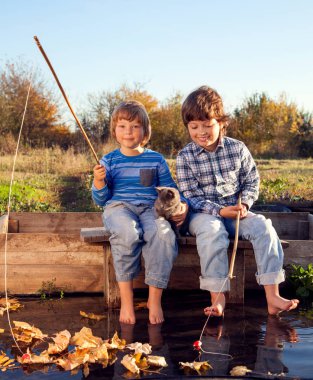 Mutlu çocuk balığa Nehri ile evde beslenen hayvan, bir çocuk ve yavru kedi Fisher üzerinde göl kıyısında bir olta ile