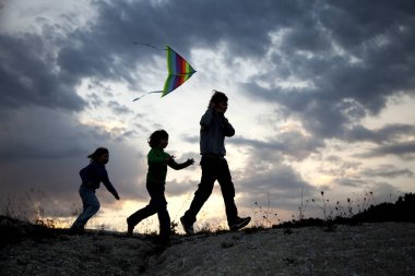 Yaz günbatımı çayır siluetüzerinde uçurtma oynayan çocuklar