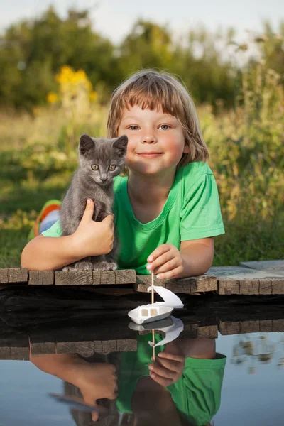 Niño y su amado gatito jugando con un barco desde muelle en estanque — Foto de Stock