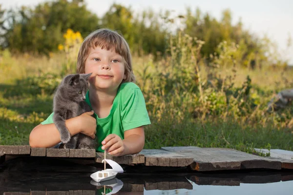 Niño y su amado gatito jugando con un barco desde muelle en estanque — Foto de Stock