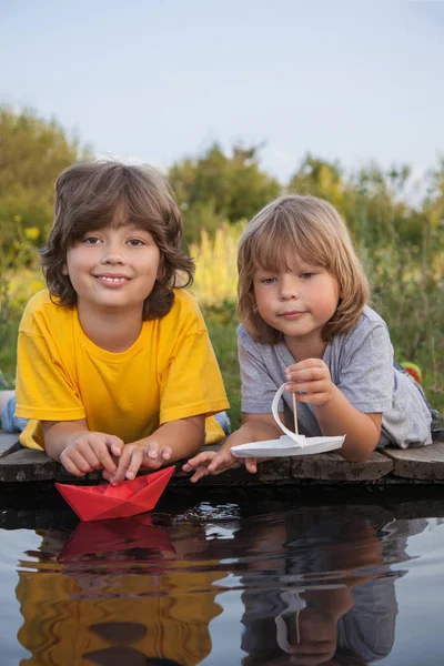 Deux garçons autorisés bateaux en papier de la jetée de la rivière — Photo