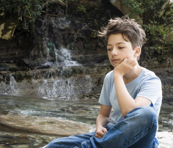 Ragazzo adolescente seduto accanto alla cascata di montagna — Foto Stock