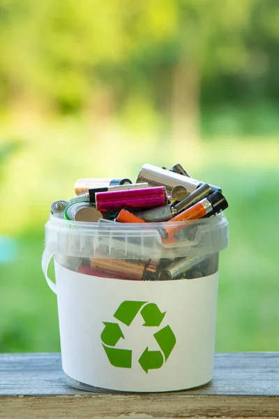 Battery recycle bin with old element on wood table on green grass background