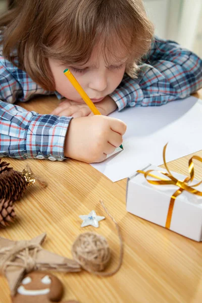 少年はサンタクロースへの手紙を書く クリスマスツリーの近くだ メリークリスマスとハッピーホリデー — ストック写真