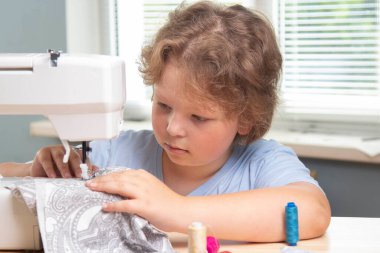 Çocuk el işi yapmak için dikiş makinesi kullanıyor.