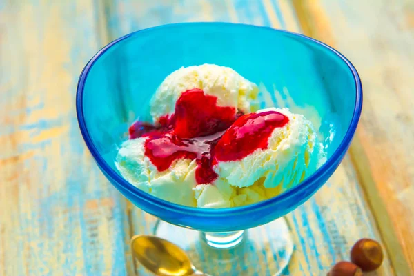 Blue bowl with ice cream and with red jam on a wooden background of boards