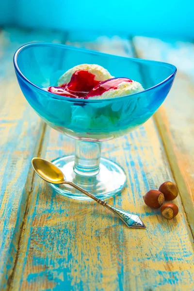 Blue bowl with ice cream and with red jam on a wooden background of boards