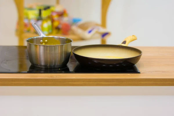 A frying pan and saucepan are on the hob in the kitchen on a colorful multi-colored background.