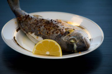 Fırında pişmiş balık Dorado baharat ve bir dilim limon beyaz bir plaka üzerinde.