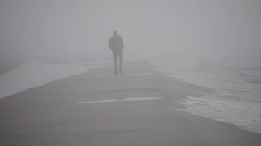 Bekar bir adam kumlu bir plaj boyunca sahil boyunca sis gider.