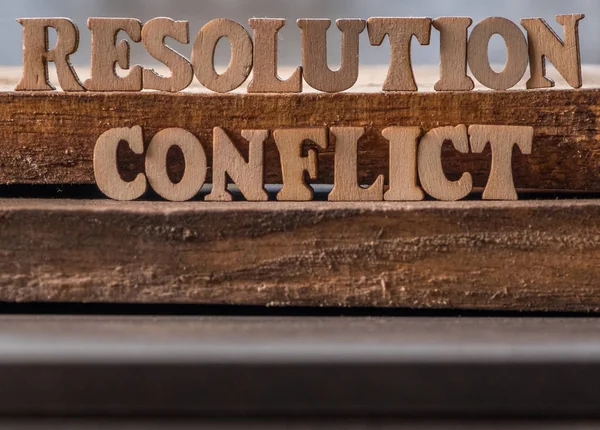 \'RESOLUTION\' and \'CONFLICT\' text on wooden background.