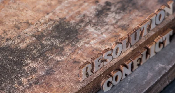 \'RESOLUTION\' and \'CONFLICT\' text on wooden background.