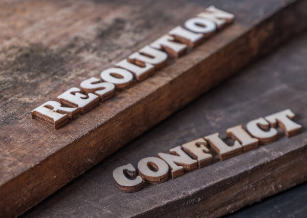 'RESOLUTION' and 'CONFLICT' text on wooden background.