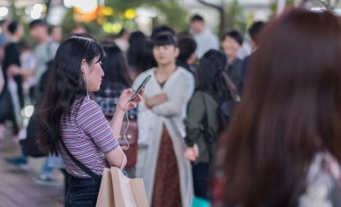 Tokyo, Japonya - 23 Haziran 2018. Hachiko Meydanı, Shibuya geceleri'akıllı telefon kullanan Japon kız.