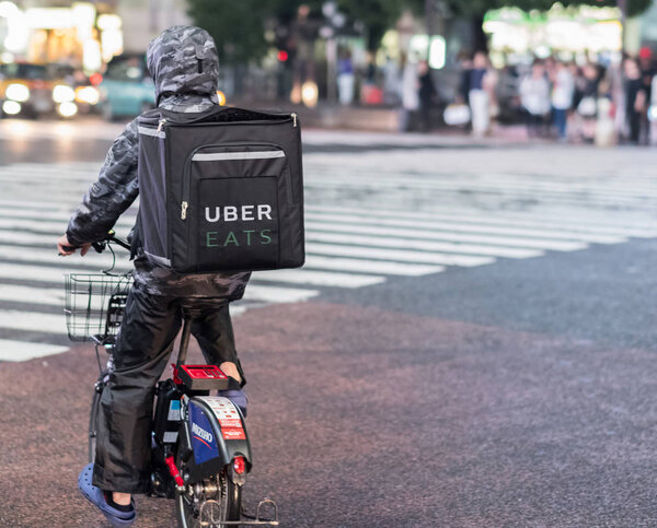 TOKYO, JAPAN - JUNE 23RD, 2018. Uber Eats food delivery services bicycle rider in the street of Shibuya at night.