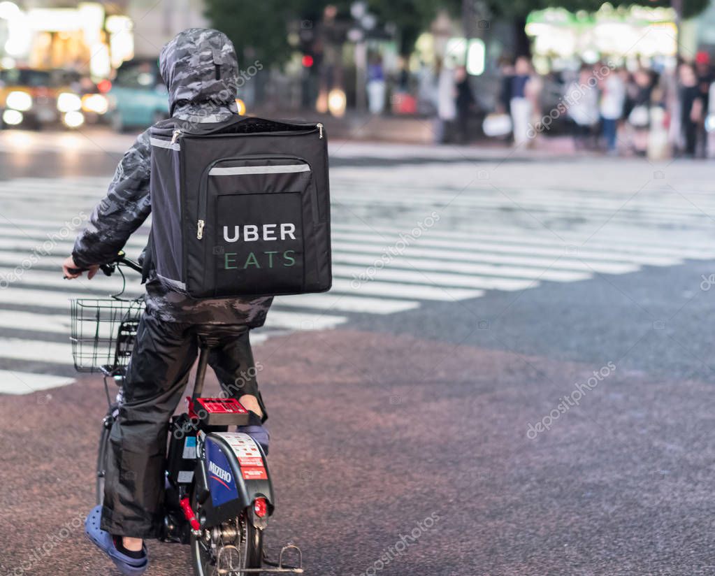 TOKYO, JAPAN - JUNE 23RD, 2018. Uber Eats food delivery services bicycle rider in the street of Shibuya at night.