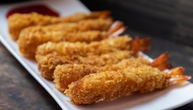 Ahşap arka plan üzerinde beyaz tabak içinde gevrek un kaplı derin kızarmış karides