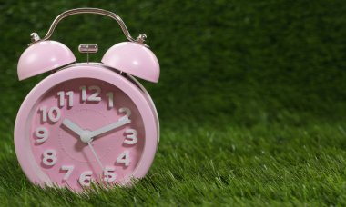 Çalar saat yeşil çimenlerin üzerinde pembe, yakın çekim