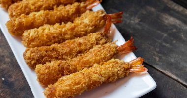 Ahşap arka plan üzerinde beyaz tabak içinde gevrek un kaplı derin kızarmış karides