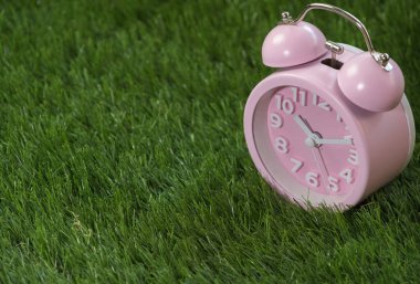 Çalar saat yeşil çimenlerin üzerinde pembe, yakın çekim